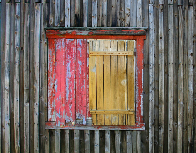Gammelt trefasade med et vindu, delvis dekket av gul og rød, avskallet maling