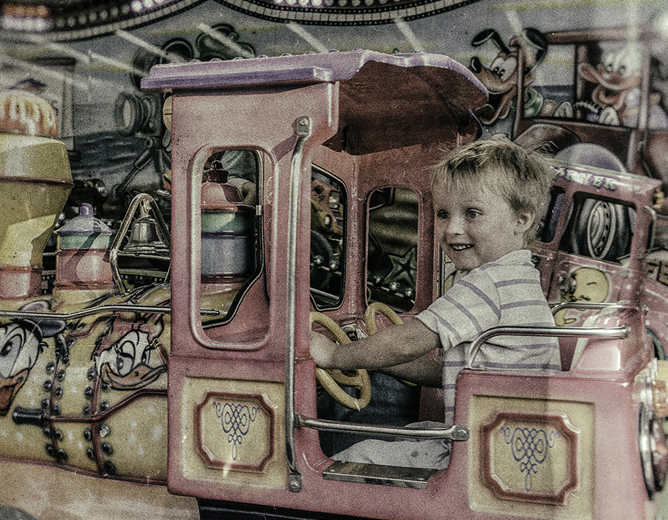 Et barn som sitter i en rosa og gul lekebil i en karusell