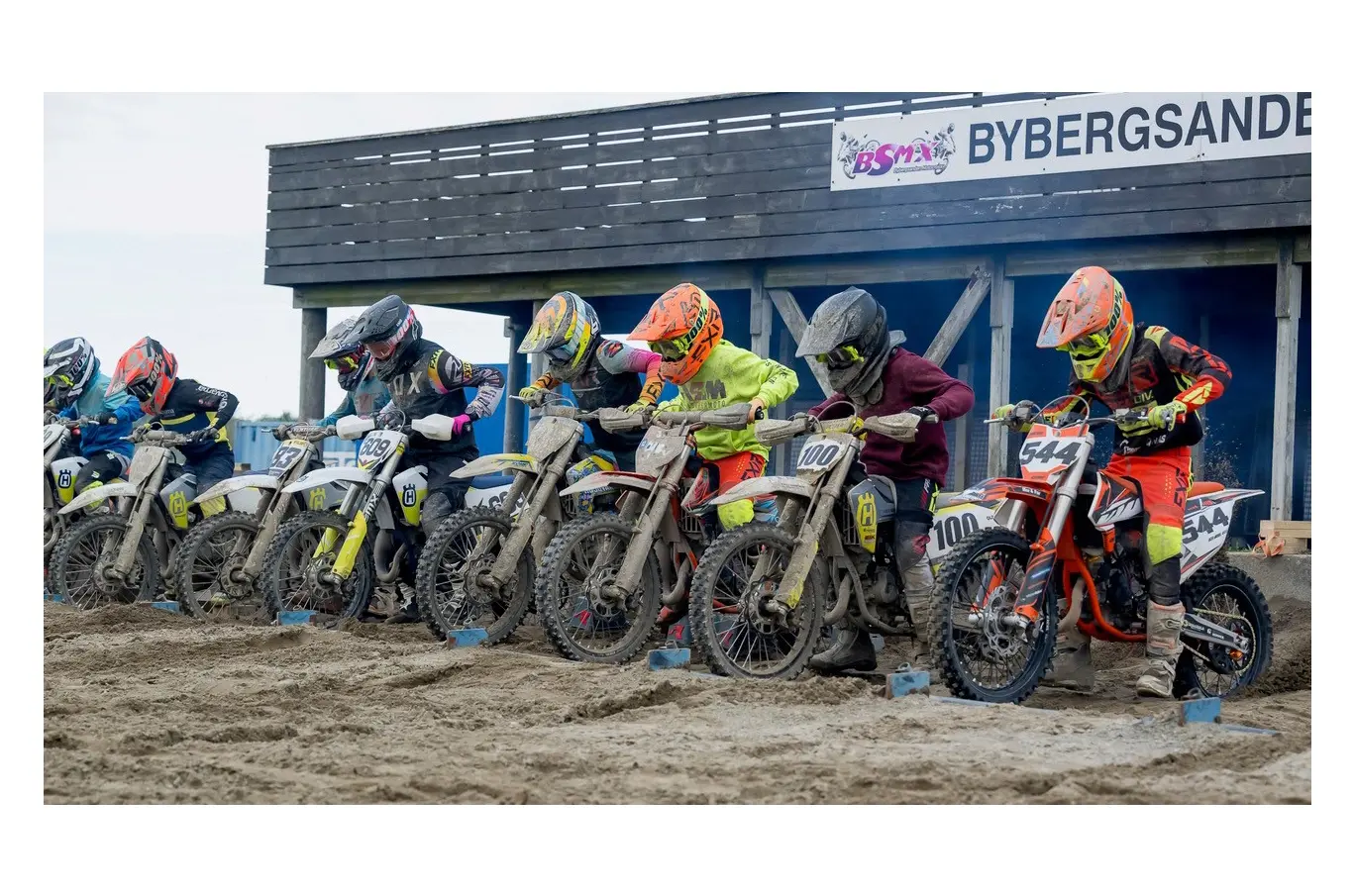 Motocrosskjørere på rekke gjør seg klare til start på en sandbane ved Bybergsanden