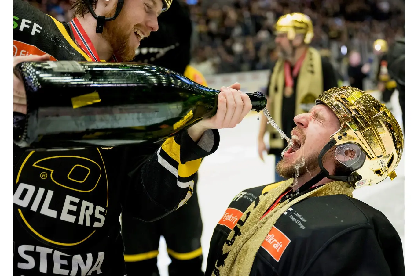 En hockeyspiller med gullhjelm får champagne helt fra en stor flaske av en lagkamerat i svarte og gule drakter.