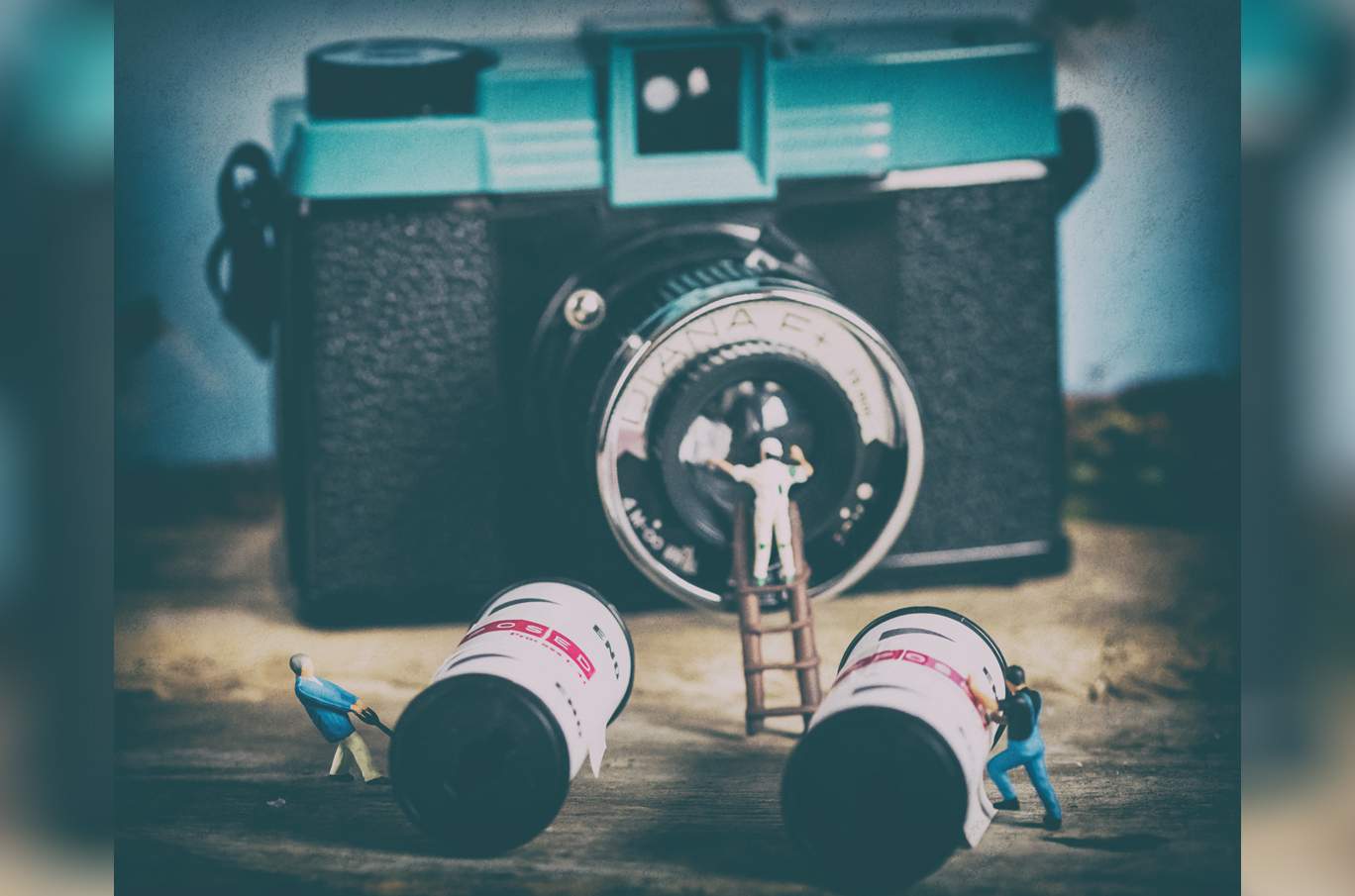 Miniatyrfigurer jobber med et gammelt kamera, en står på en stige foran linsen, mens to dytter filmruller