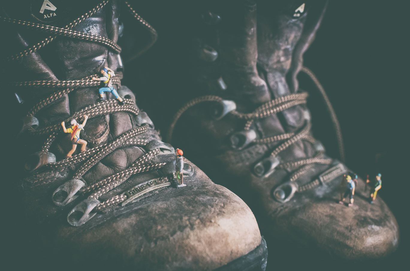 Miniatyrfigurer klatrer på snørelisser til et par slitne fjellstøvler