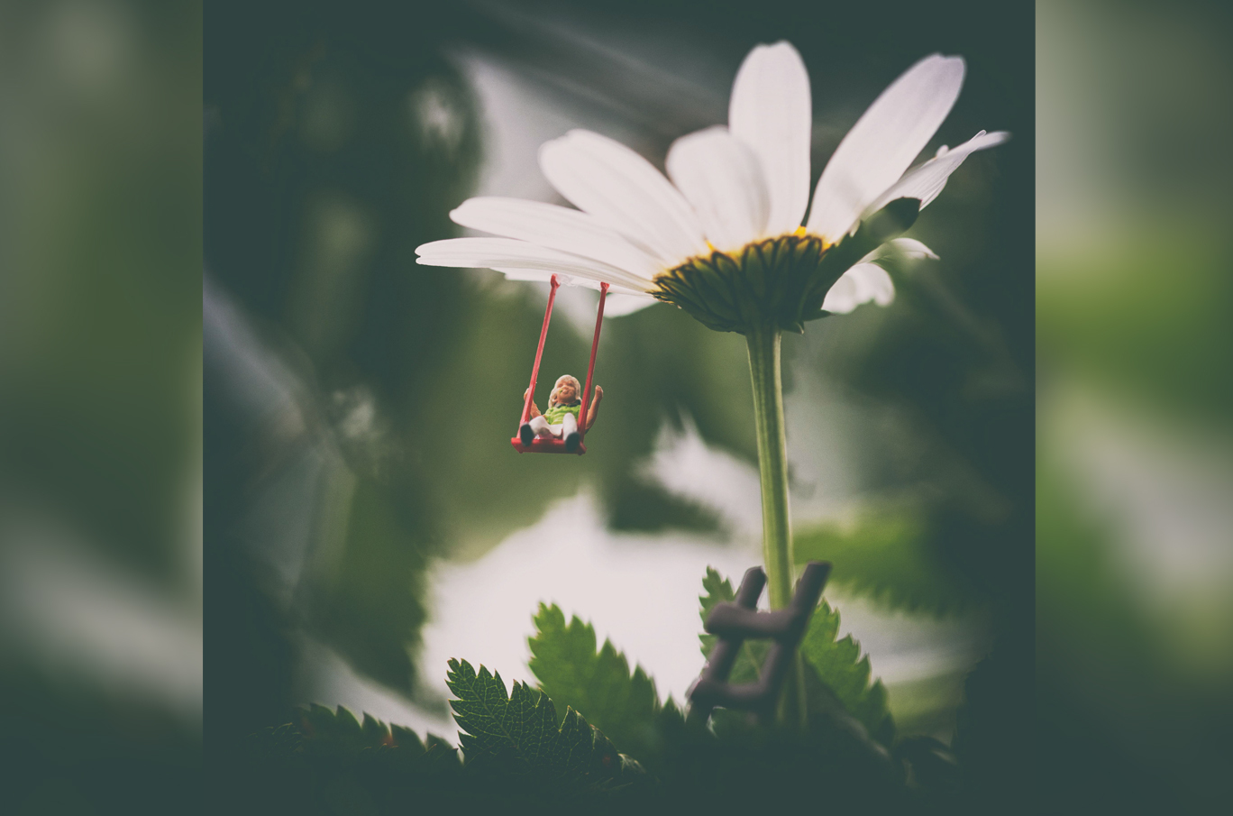 Liten figur av en jente som sitter på en rød huske festet til en hvit prestekrage-blomst