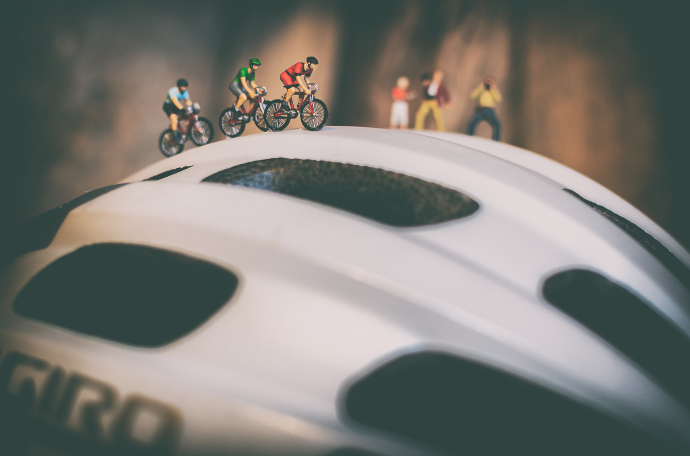 Små sykkelryttere sykler over en stor, hvit sykkelhjelm