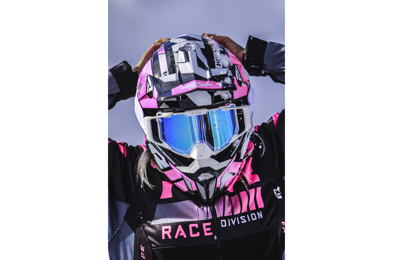 Snøscooterfører med rosa og svart hjelm, blåbriller og snøflekker justerer hjelmen med begge hender