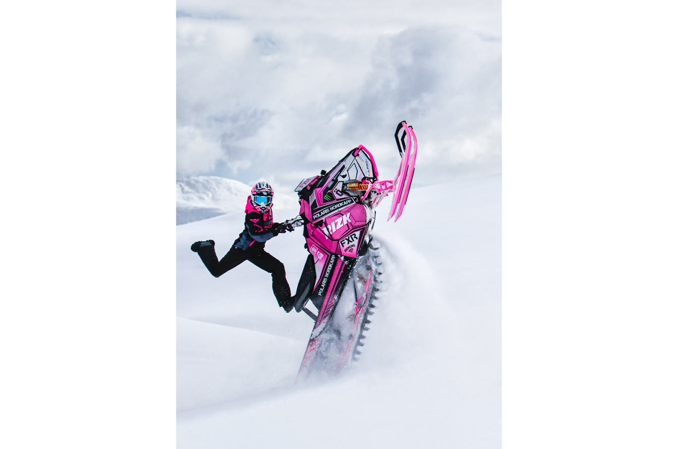 Person som kjører en rosa snøscooter i høy fart gjennom snødekt landskap, snøsprut i luften