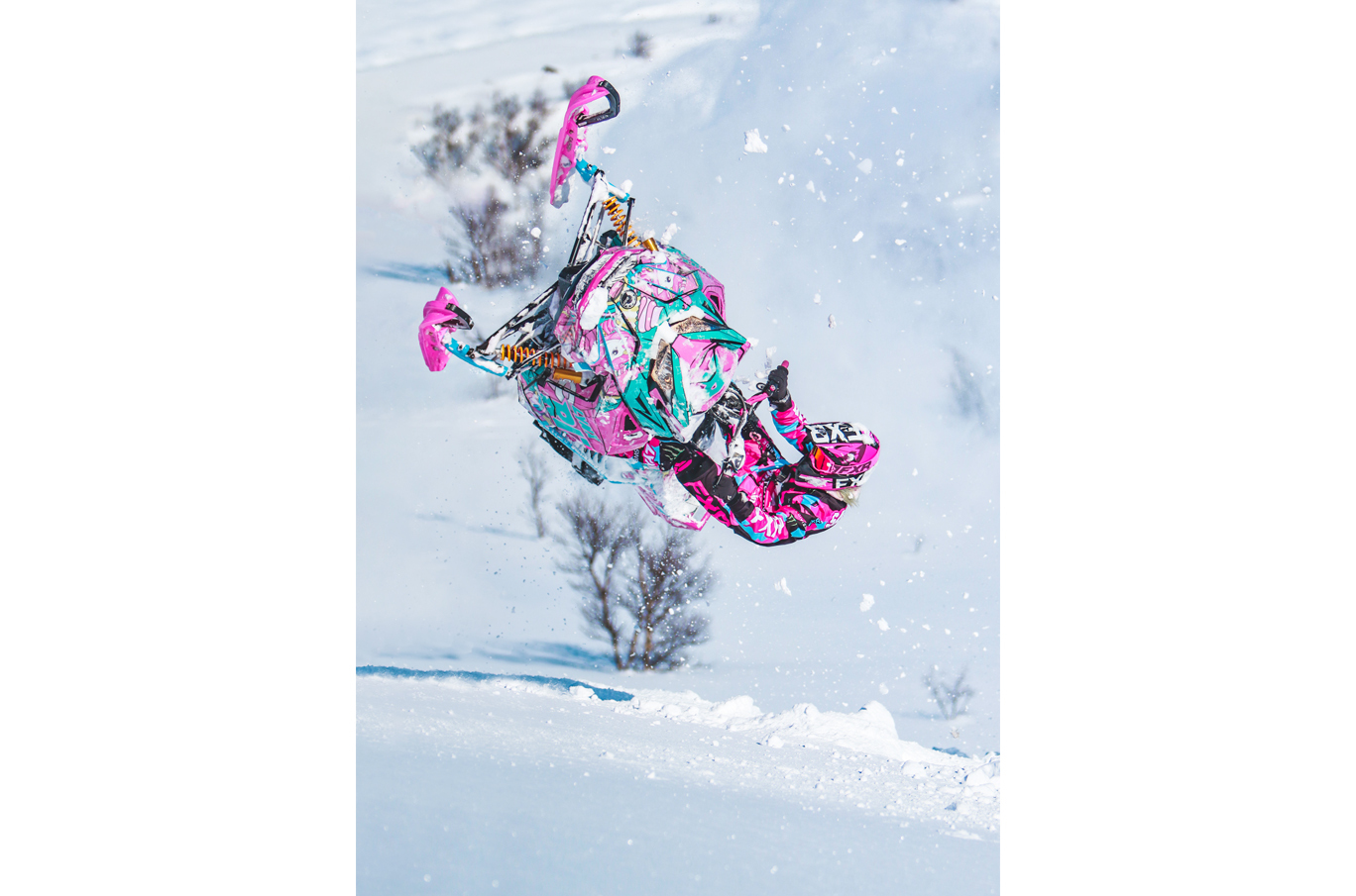 En person utfører et luftig snøskutersprang med en fargerik snøskuter i rosa, turkis og hvitt