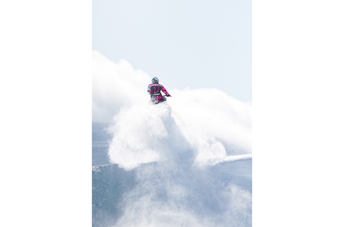 En person kjører en scooter gjennom dyp snø, omgitt av hvit snørøyking i et klart vinterlandskap