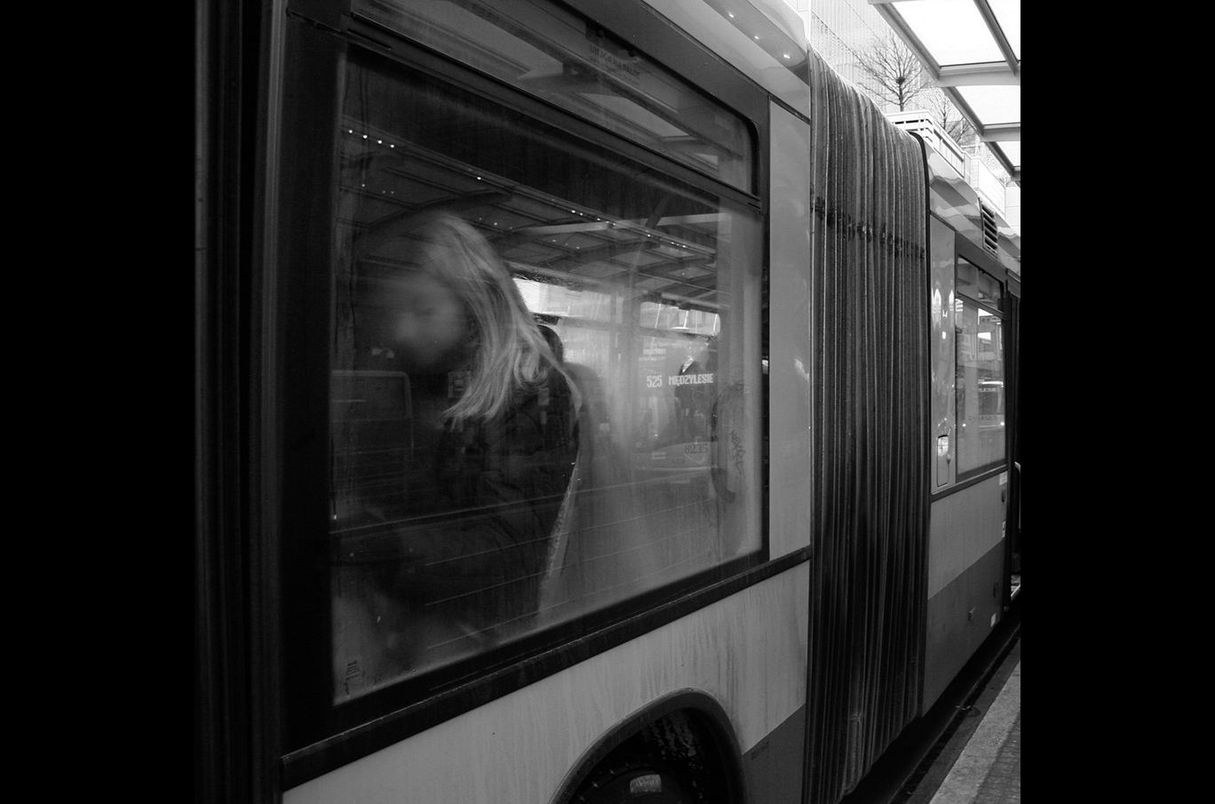 Person med langt lyst hår står inne i en trikk mens den står ved en stasjon.