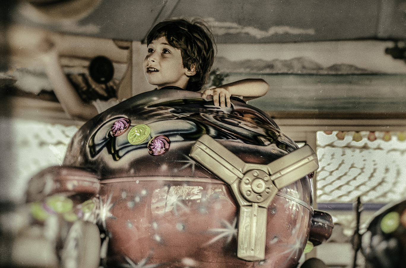 Barn som sitter i en fargerik karusell formet som en romrakett med detaljer i metallstiler og stjerner