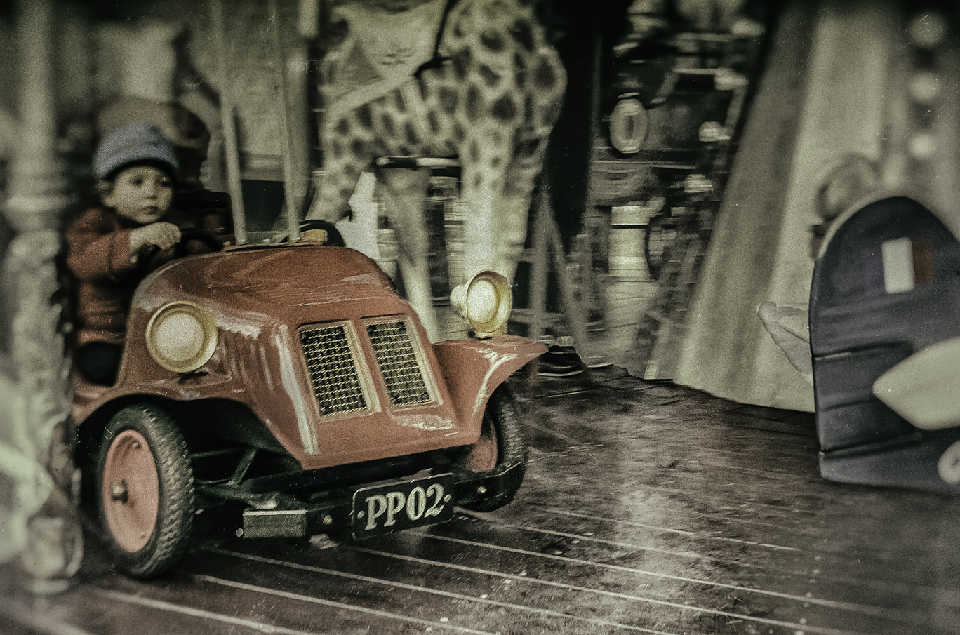 Et rødt lekebil på en gammeldags karusell med detaljer av en sjiraff i bakgrunnen