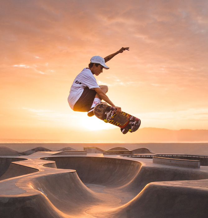 En person som gjør et skateboard-triks over en moderne skatepark i solnedgangens varme lys