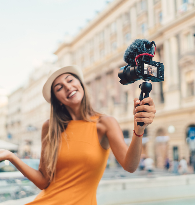 Kvinne i oransje kjole filmer seg selv med et kamera på en stabilisator, bymiljø i bakgrunnen