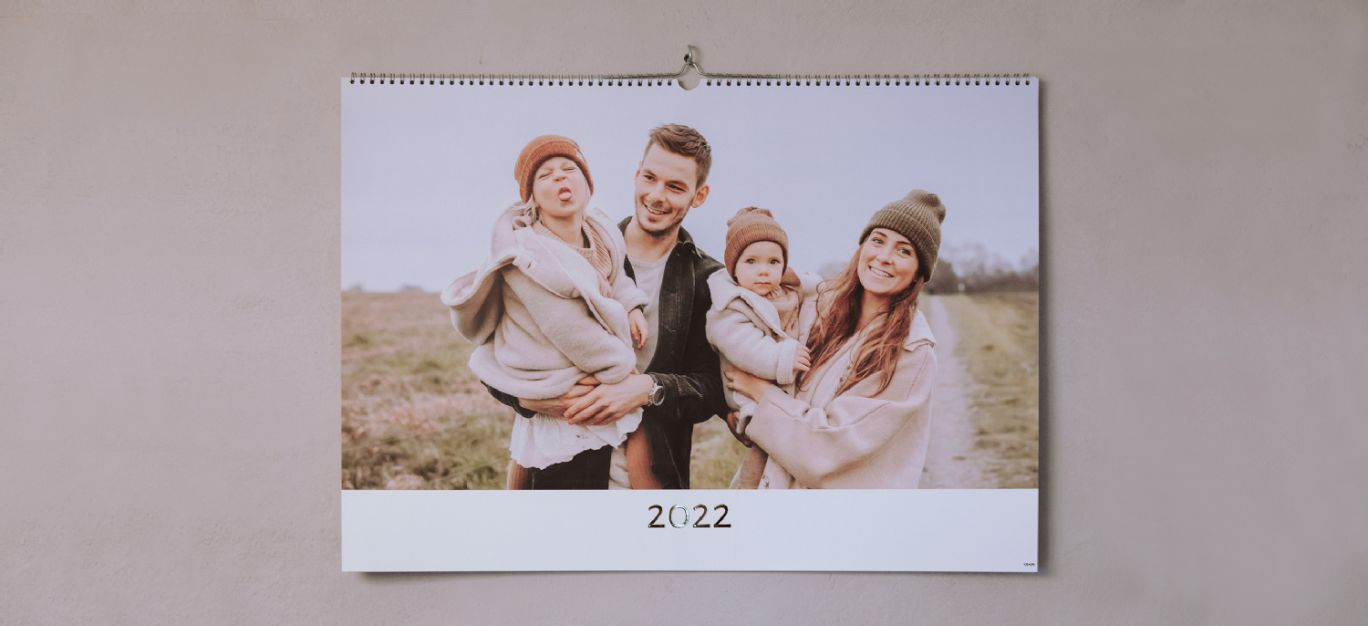 En vegghengt kalender med familiebilde, omgitt av en myk og naturlig bakgrunn