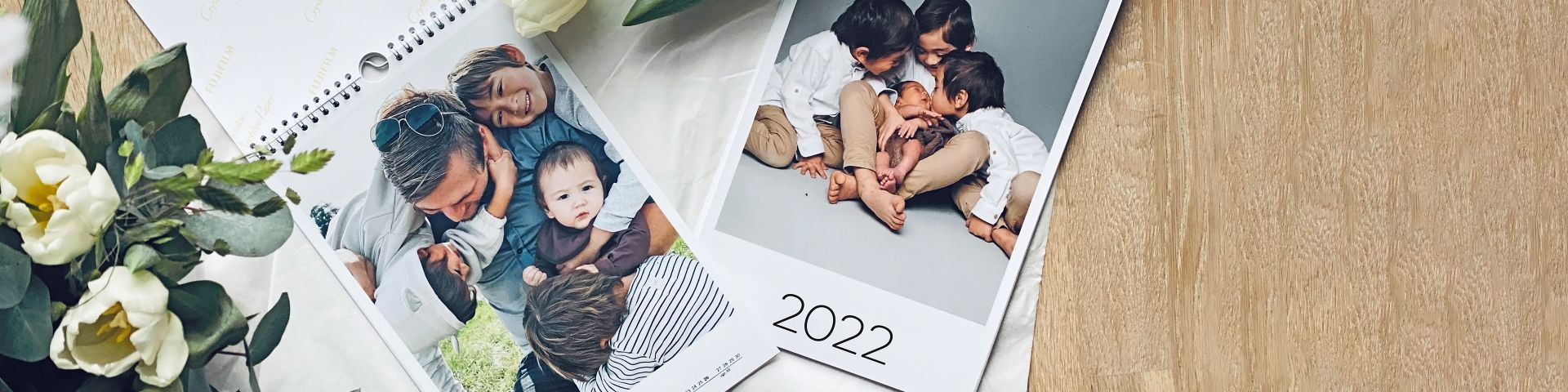 To kalendere med familiebilder, omgitt av hvite blomster på en treoverflate