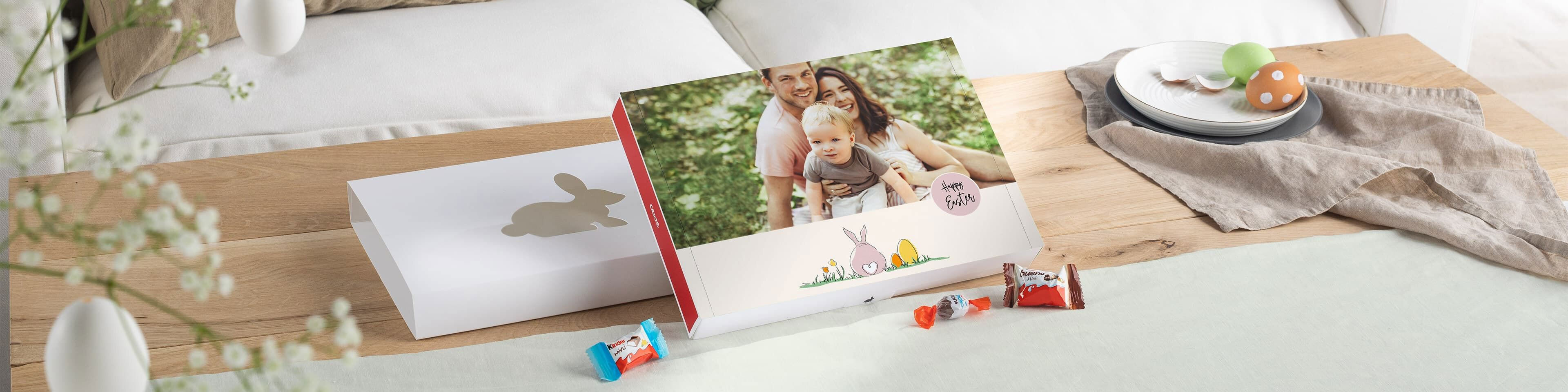 Fotobok med påsketema på et trebord, dekorert med sjokolade, fargerike egg og vårblomster