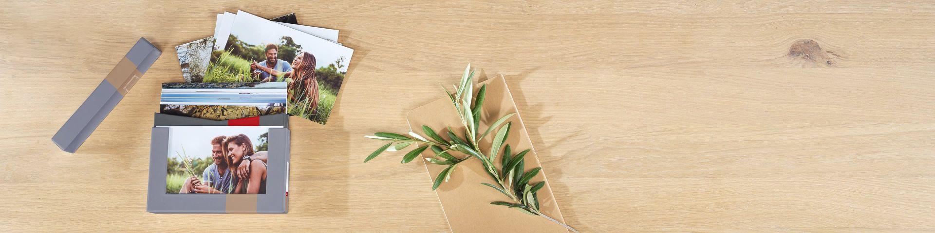 Fotoprint i en stabel sammen med olivengren og naturlig konvolutt på lyst trebord