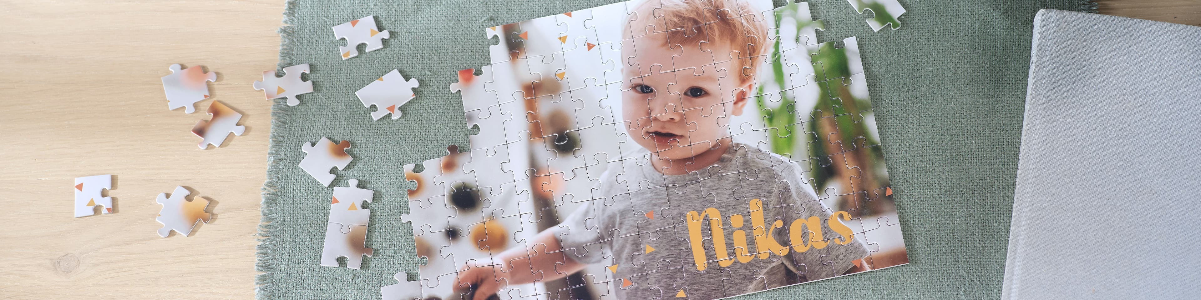 Et delvis fullført puslespill med navnet "Nikas" i gule bokstaver på et lyst trebord, omgitt av løse puslespillbrikker.