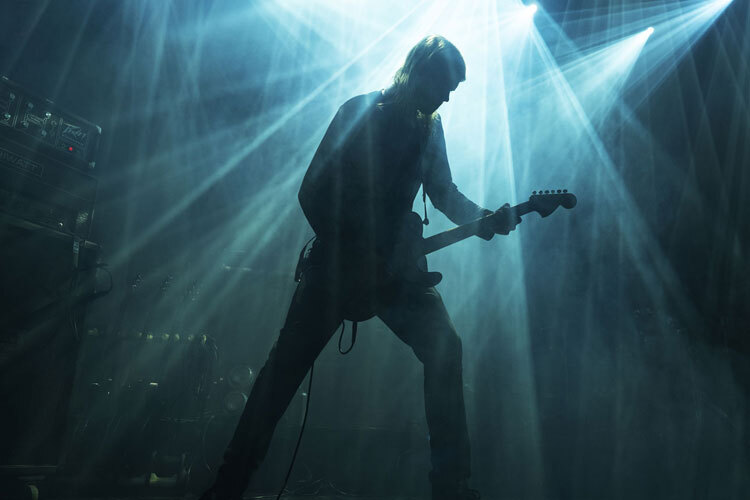 En gitarist spiller på en scene i dramatisk lysshow med stråler av hvitt og blått lys En gitarist spiller på en scene i dramatisk lysshow med stråler av hvitt og blått lys