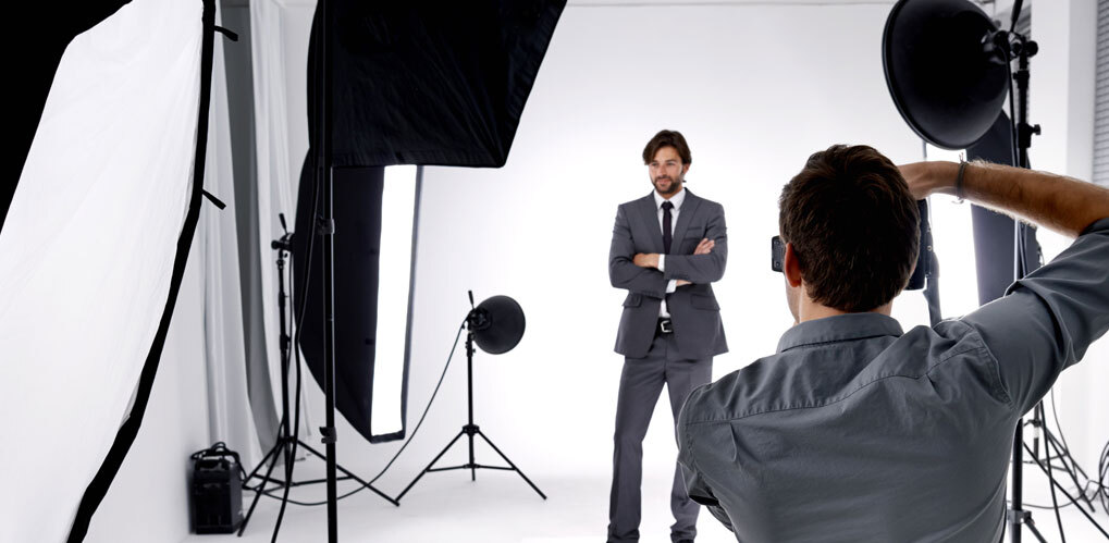 En mann i dress står med armene i kors i et profesjonelt fotostudio opplyst av flere store lamper og bakgrunnsutstyr En mann i dress står med armene i kors i et profesjonelt fotostudio opplyst av flere store lamper og bakgrunnsutstyr