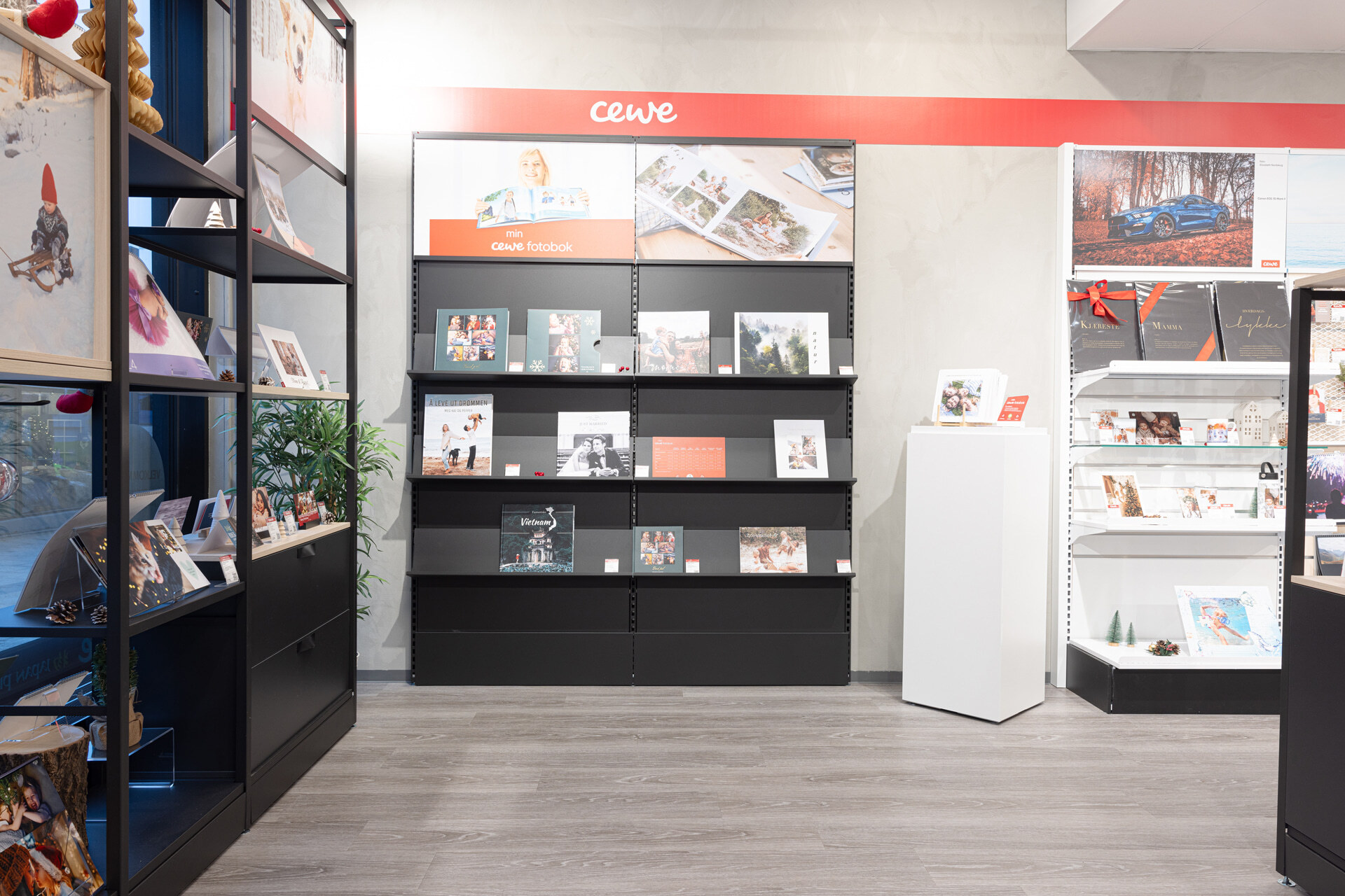 En hylle med CEWE fotobøker, rammer og andre fotoprodukter, omgitt av dekorative elementer og belysning. En hylle med CEWE fotobøker, rammer og andre fotoprodukter, omgitt av dekorative elementer og belysning.