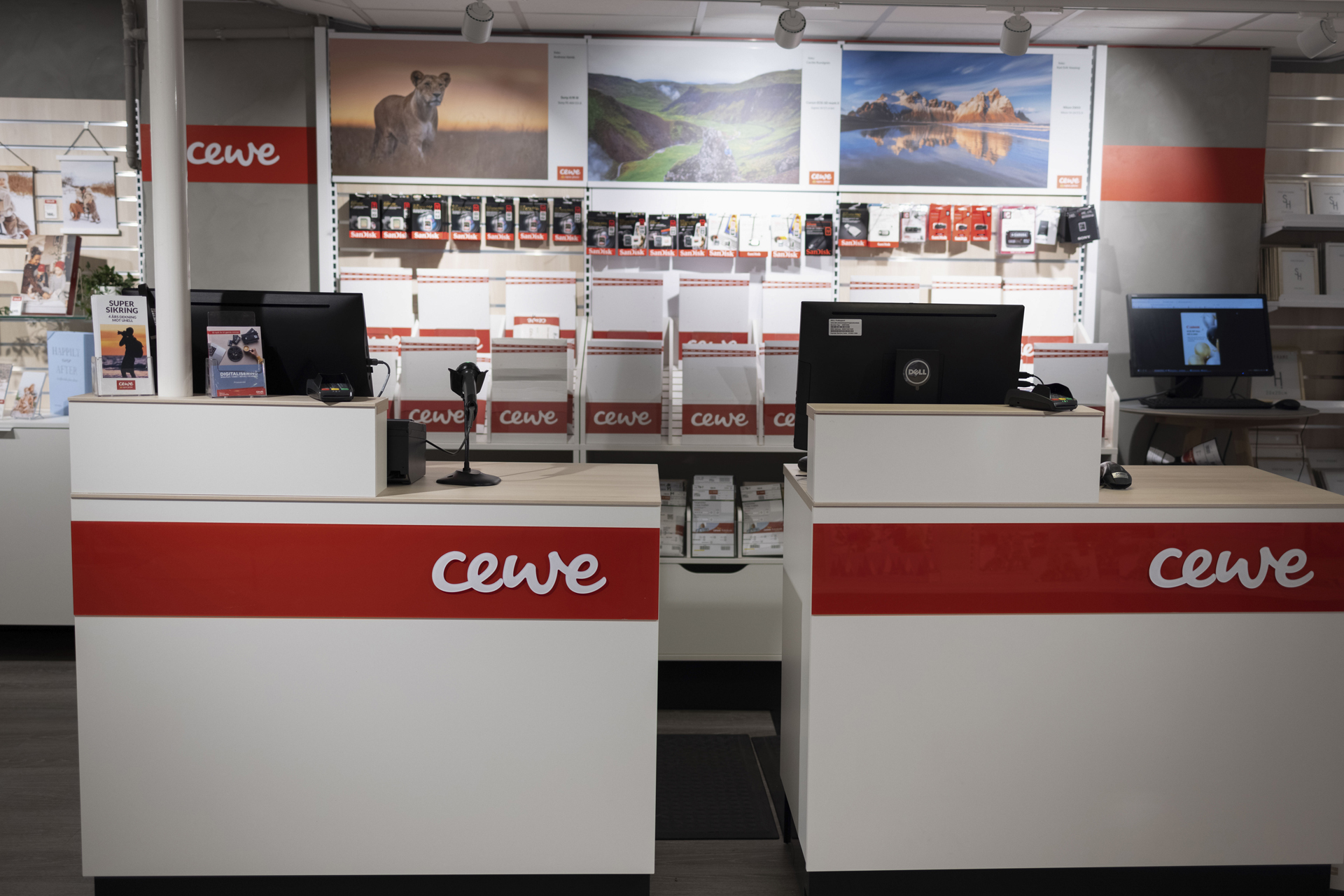 To skranker med CEWE-logo, båret av moderne design i hvitt og rødt, omgitt av produkter og veggdekorasjoner To skranker med CEWE-logo, båret av moderne design i hvitt og rødt, omgitt av produkter og veggdekorasjoner