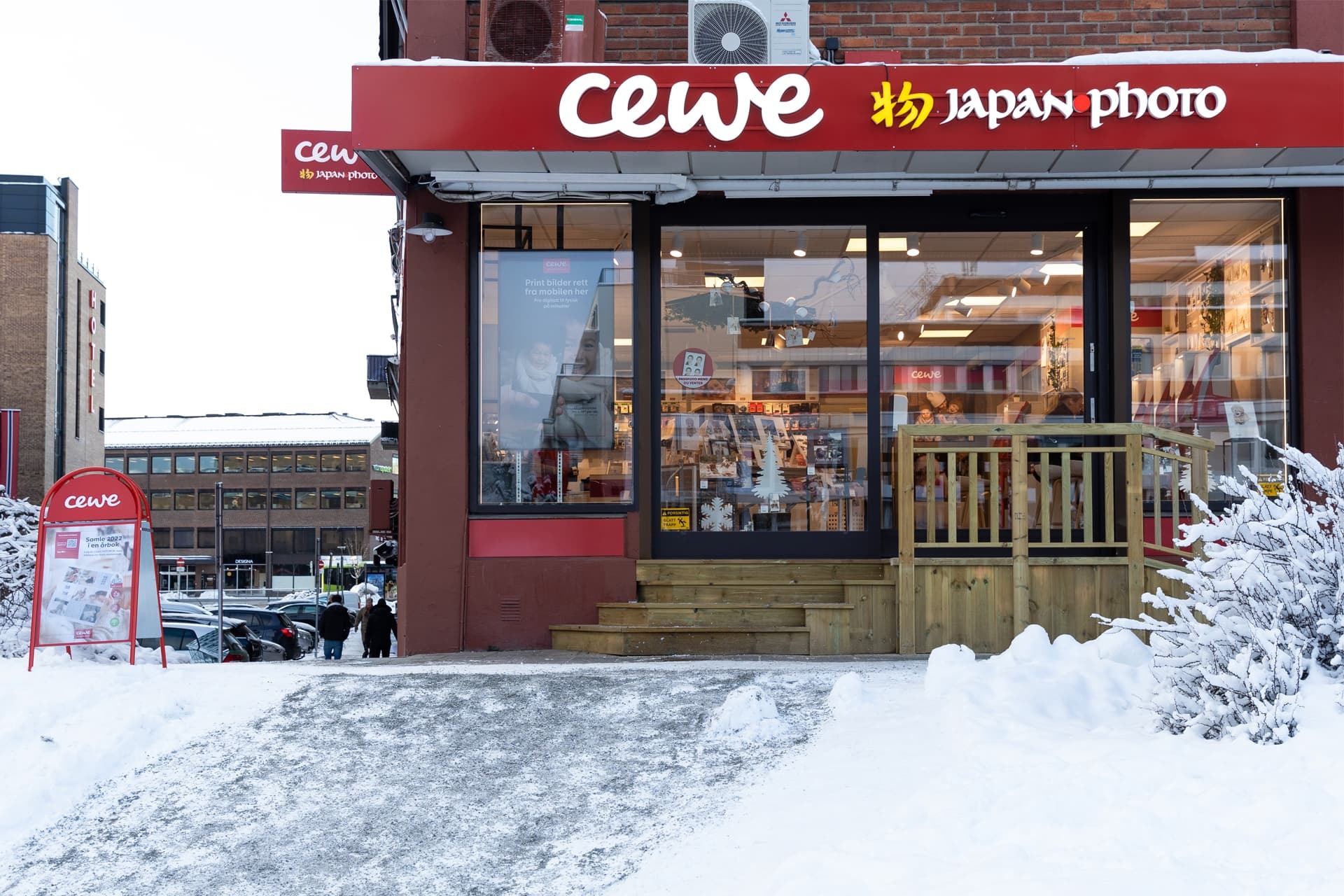 Rød butikkfasade med CEWE Japan Photo-logo, inngang med tretrapp, snødekt fortau