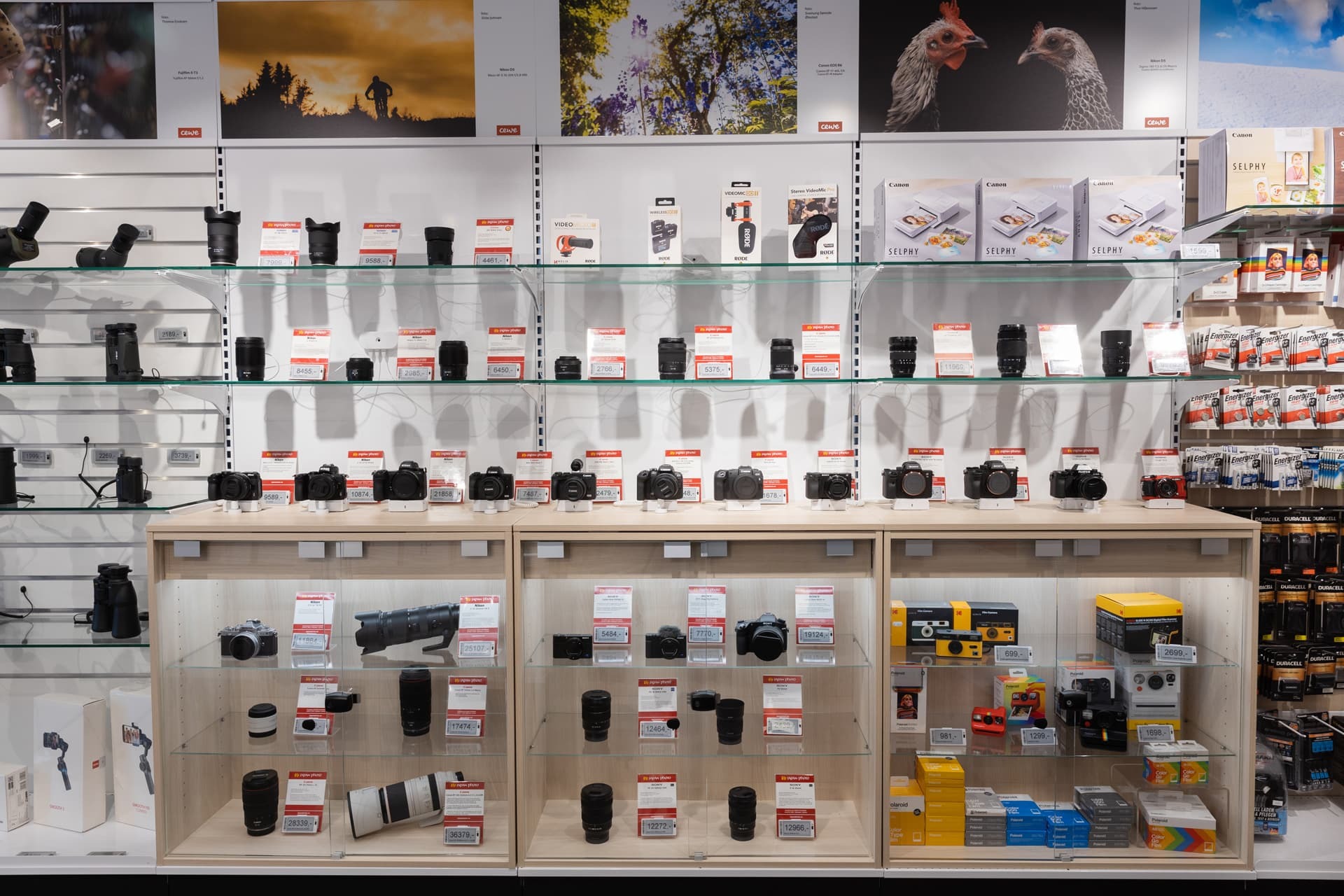 Utstillingshylle med kameraer, linser og tilbehør til salgs, med tydelige prislapper og produktbeskrivelser