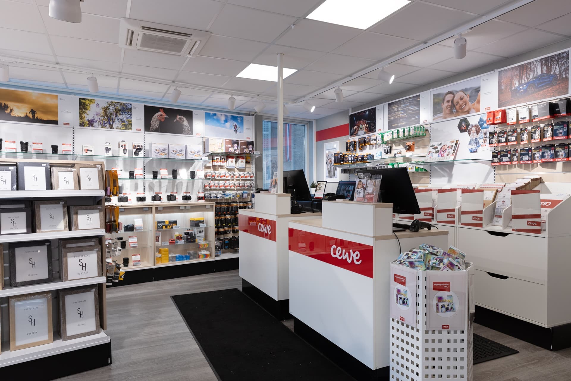 En lys og moderne CEWE-butikk med rammer, kamerautstyr og fotoprodukter pent organisert på hyller og vegger