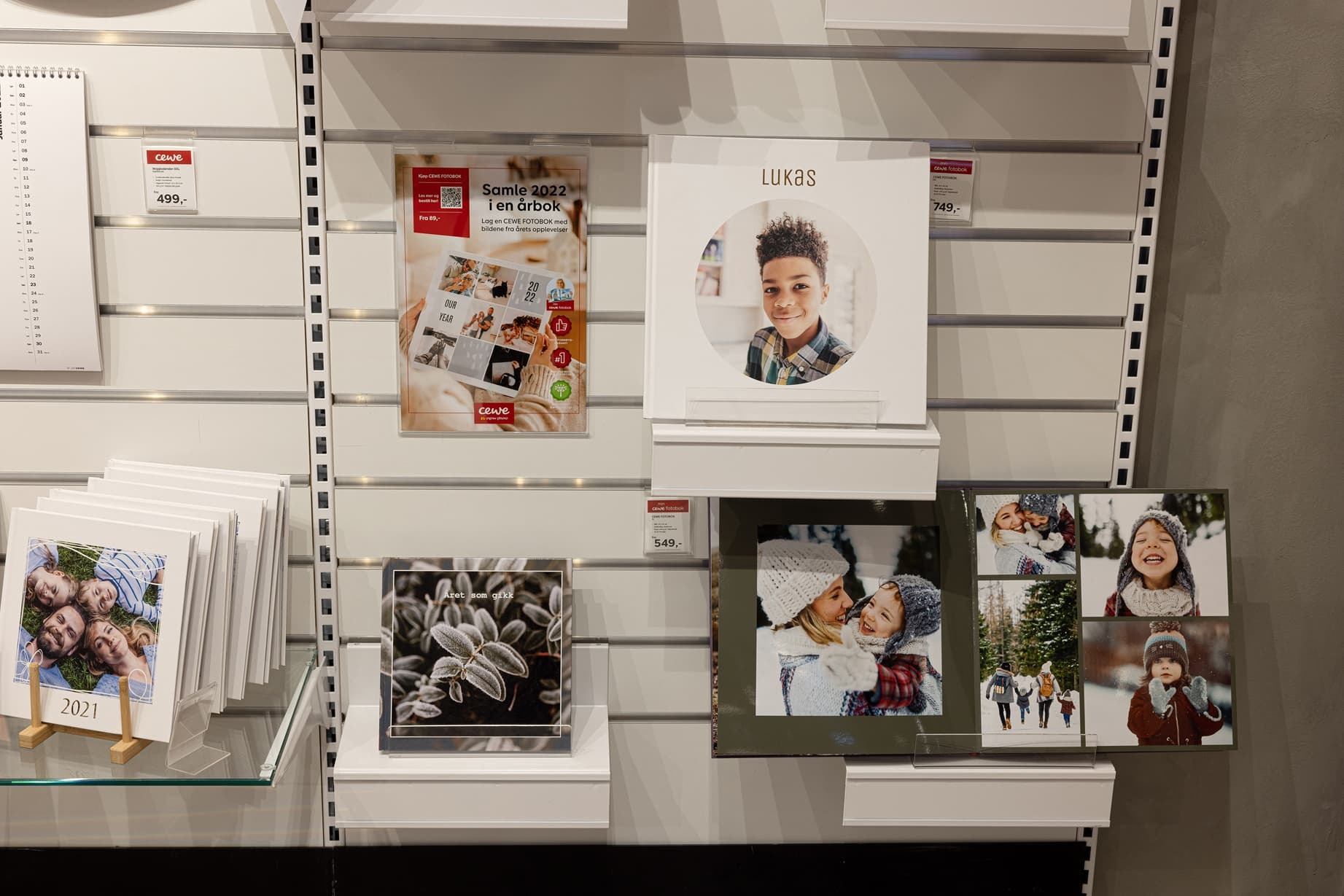 Fotobøker, kalendere og innrammede bilder utstilt på en hylle, med et lyst og moderne design.