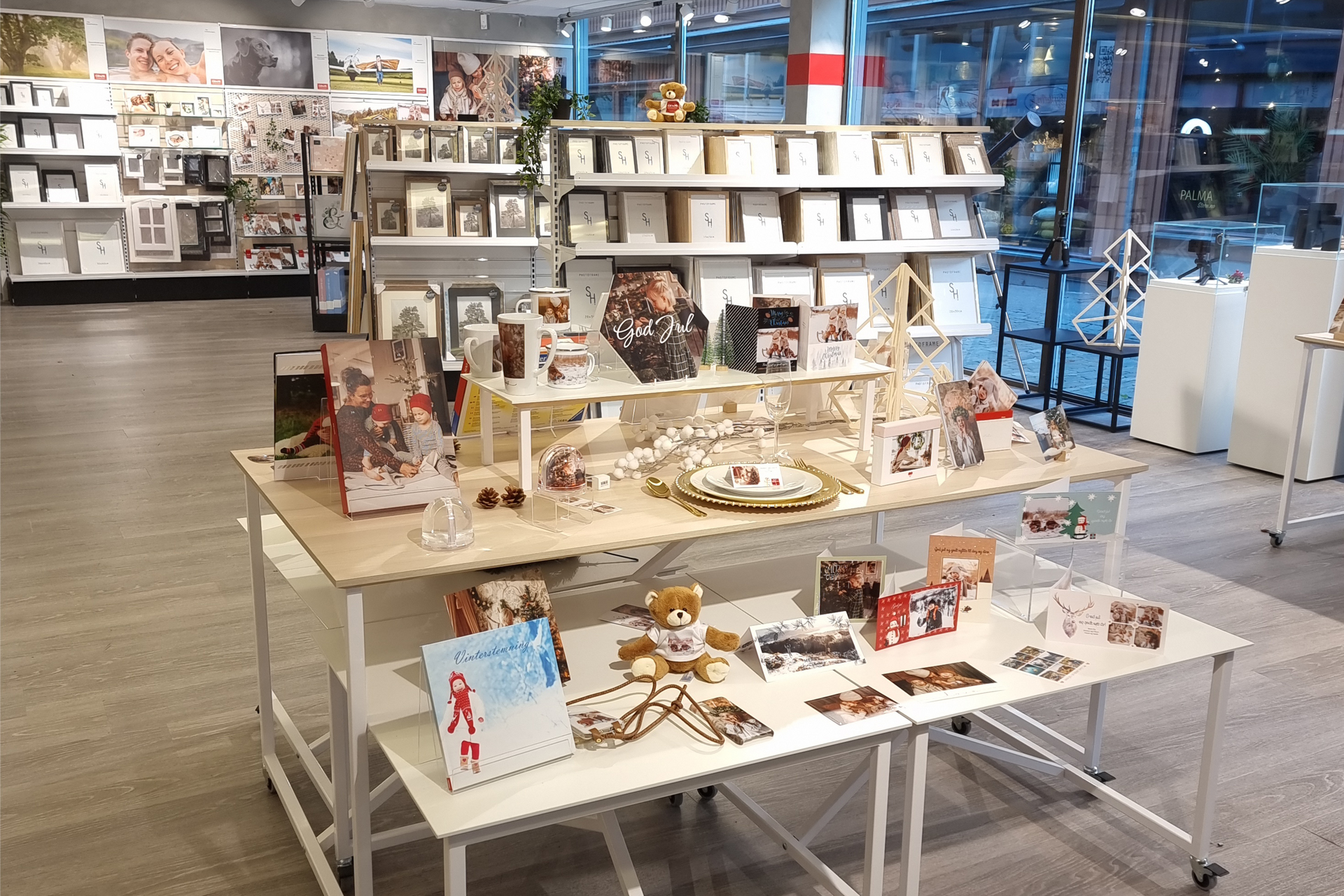 Utstilling av julekort, fotobøker, personlige gaver og dekorasjoner på et bord i en moderne butikk.