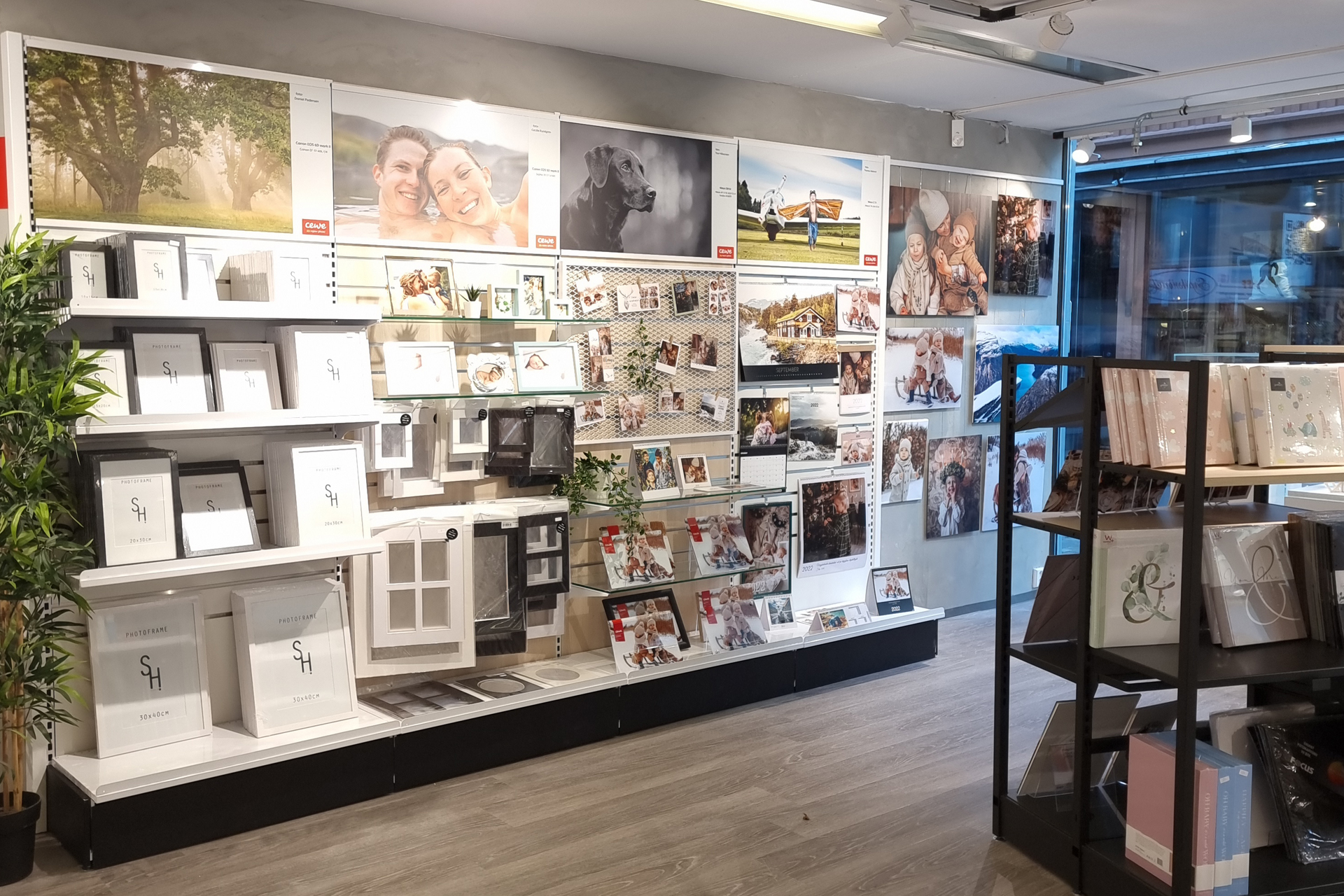 Butikkhylle med fotorammer, fotoalbum og personlig tilpassede fotogaver, dekorert med inspirerende bilder på veggen