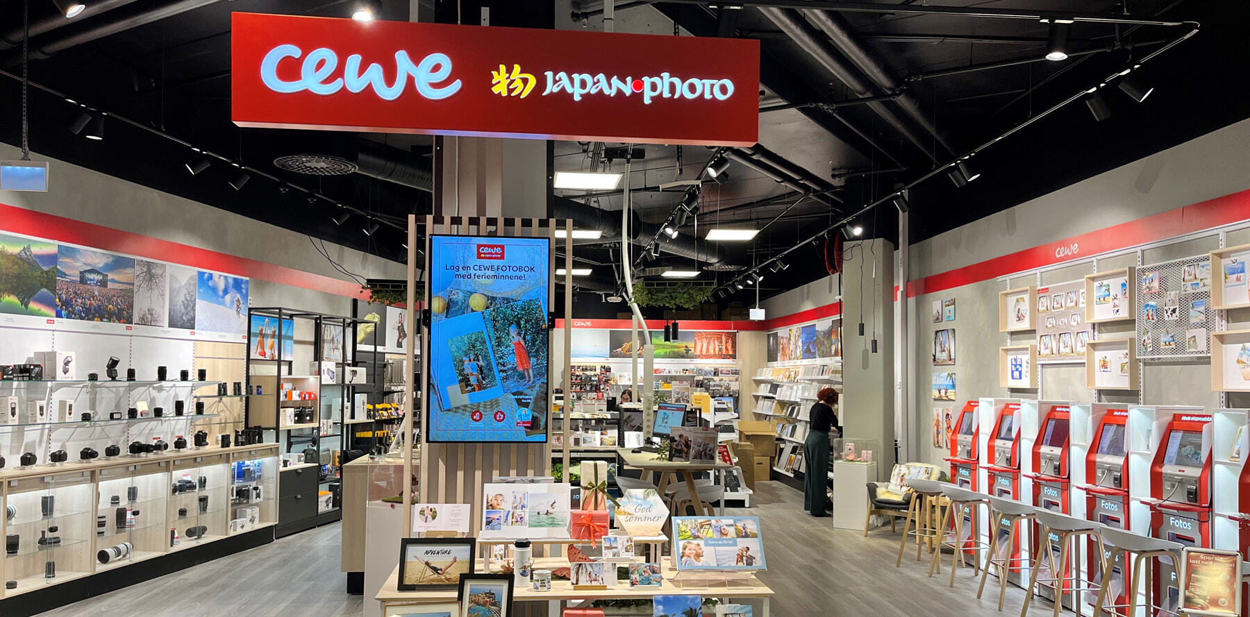 En lys og innbydende CEWE-butikk med fotoprodukter, utstyr og fotoautomater på rad