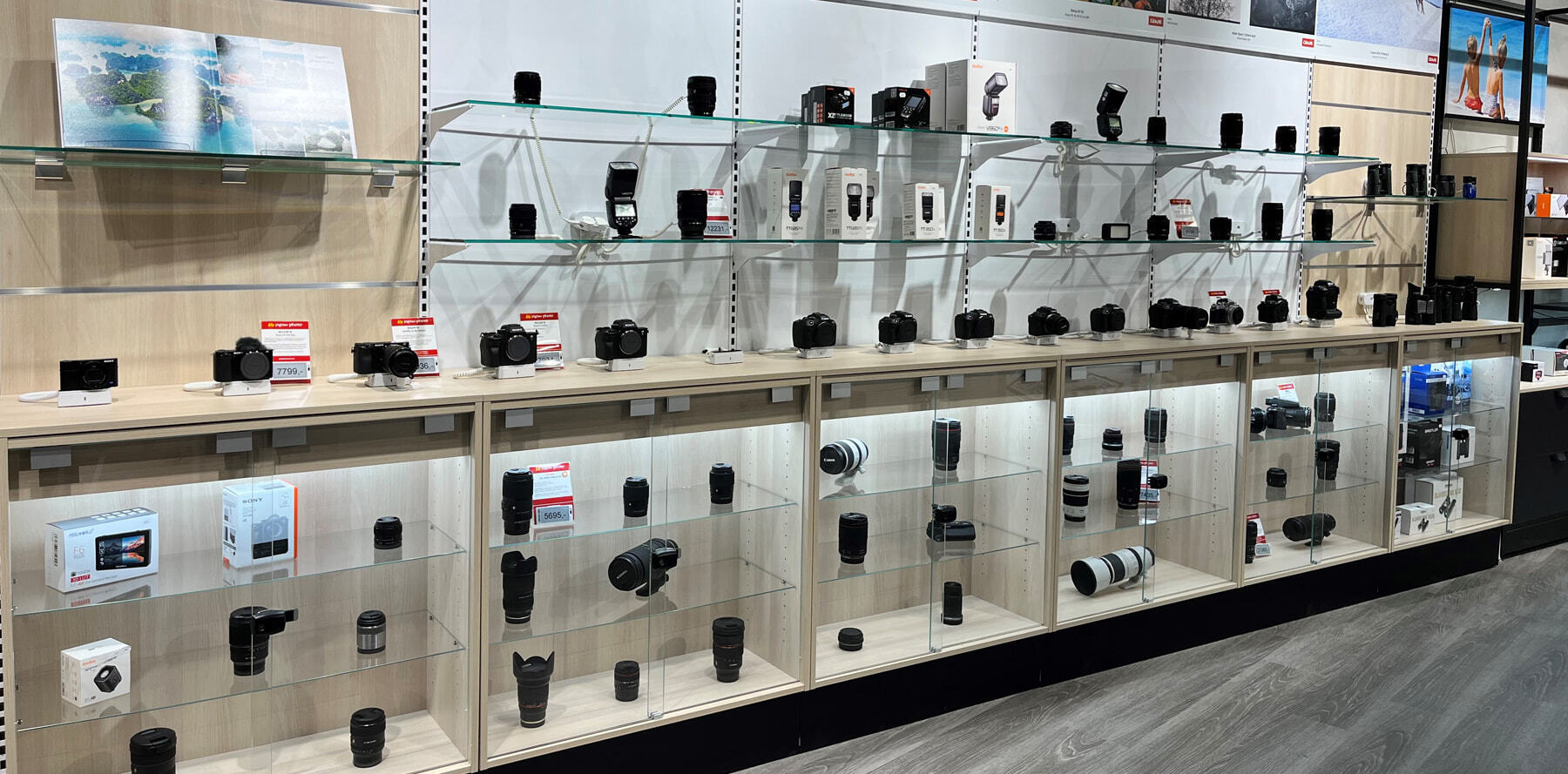 Hyller med kameraer, objektiver og fototilbehør i en butikk, opplyst med glassmontere