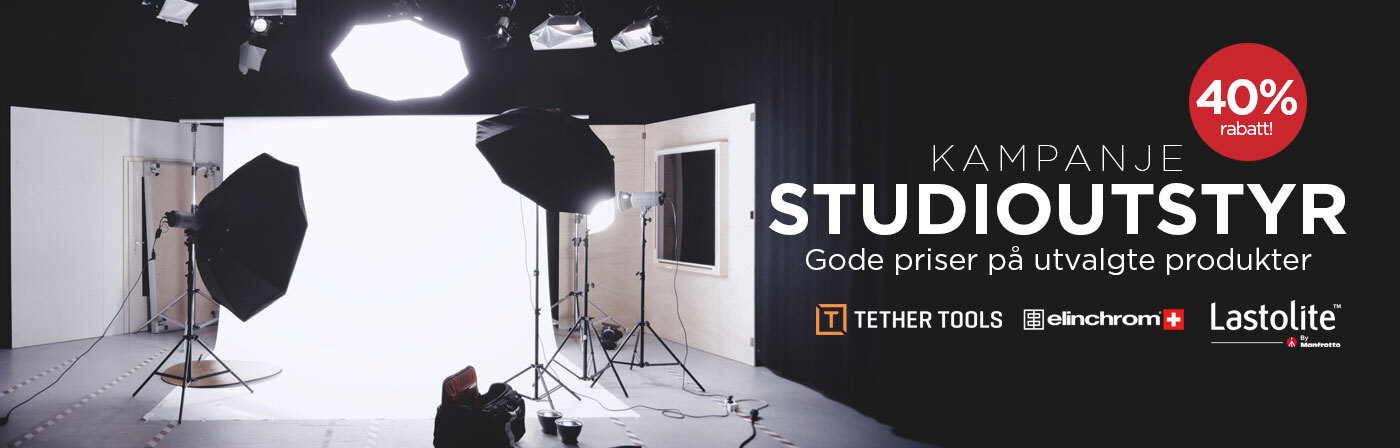 Fotostudio med profesjonelt utstyr, inkludert lysstativer, reflektorer og paraplyer som står foran en hvit bakgrunn.