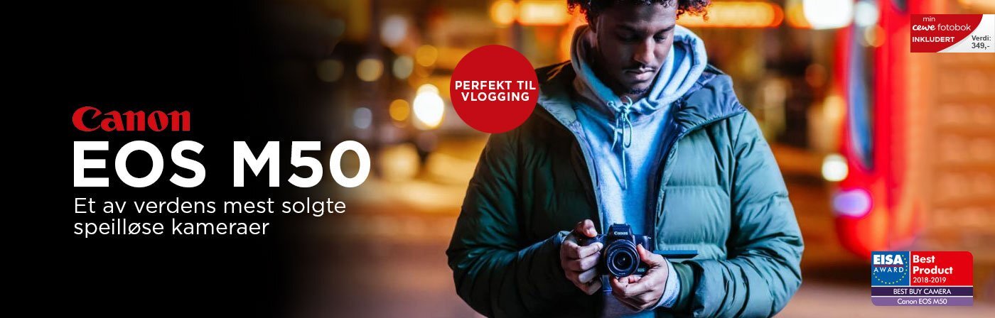 Canon EOS M50 kamera holdt i hender av en person i en by med uskarpt nattlys i bakgrunnen