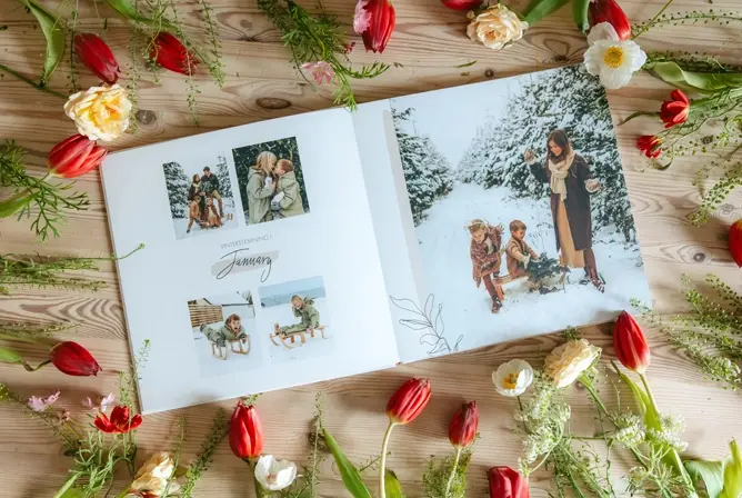 Fotoalbum med familiebilder, omringet av fargerike tulipaner og delikate blomsterdekorasjoner på trebord