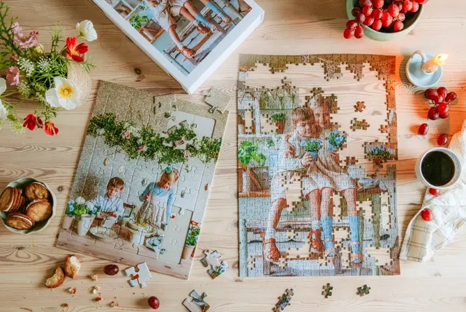Et puslespill med blomstermotiv halvferdig lagt på trebord, omgitt av blomster, kaffe, stearinlys og småkaker
